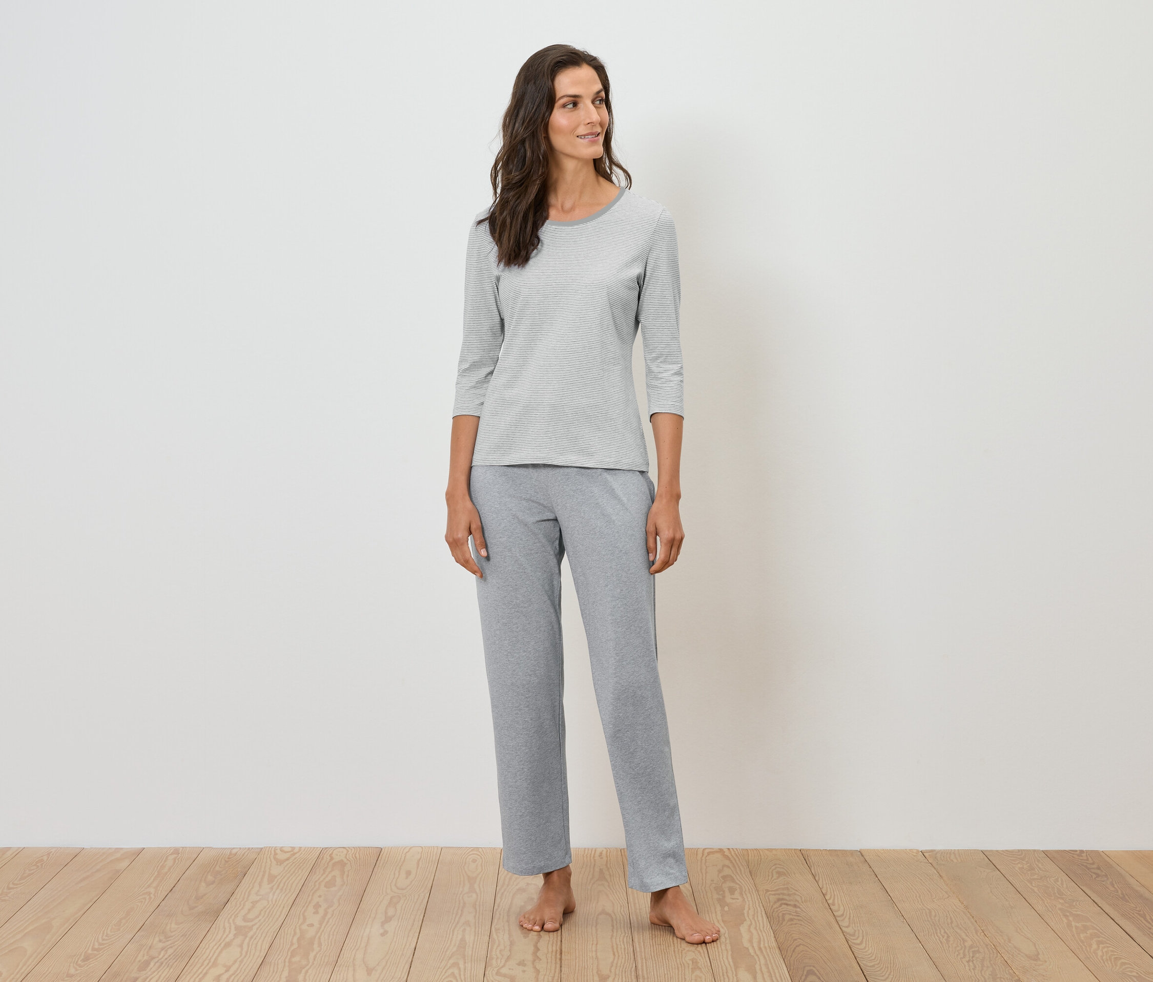 Žena stojí a má na sobě šedé pyžamo.