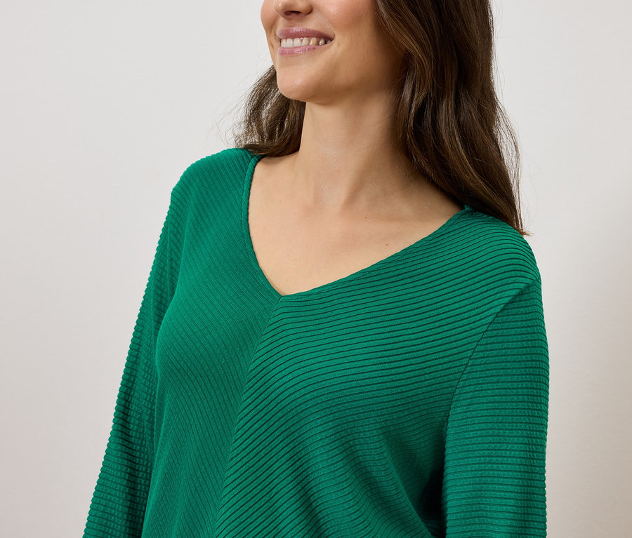 Žena s hnědými vlasy usměvavá na sobě zelený svetřík s výstřihem do V.