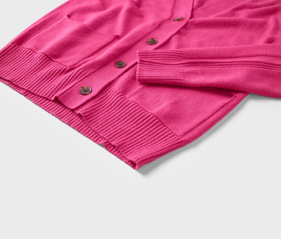 Detail růžového svetru s knoflíky a kapsou.