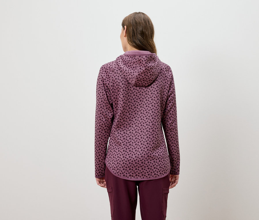 Žena v bordó soupravě s kapucí a vzorem zvířecí kůže, otočená zády.