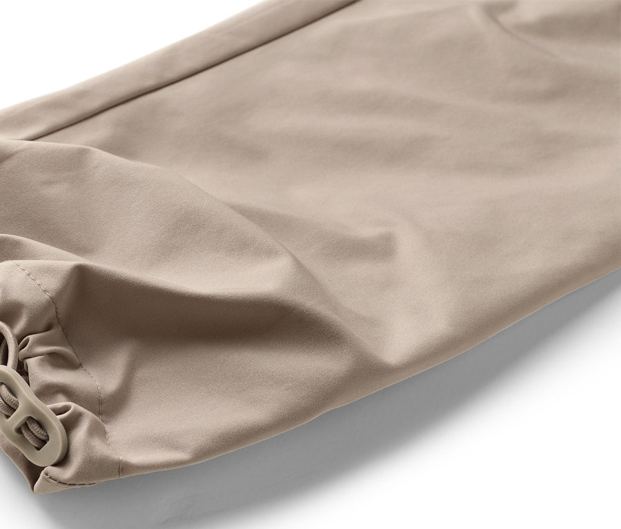 Detailní záběr na spodní část béžových kalhot s elastickým pasem a zarážkou na šňůrce.