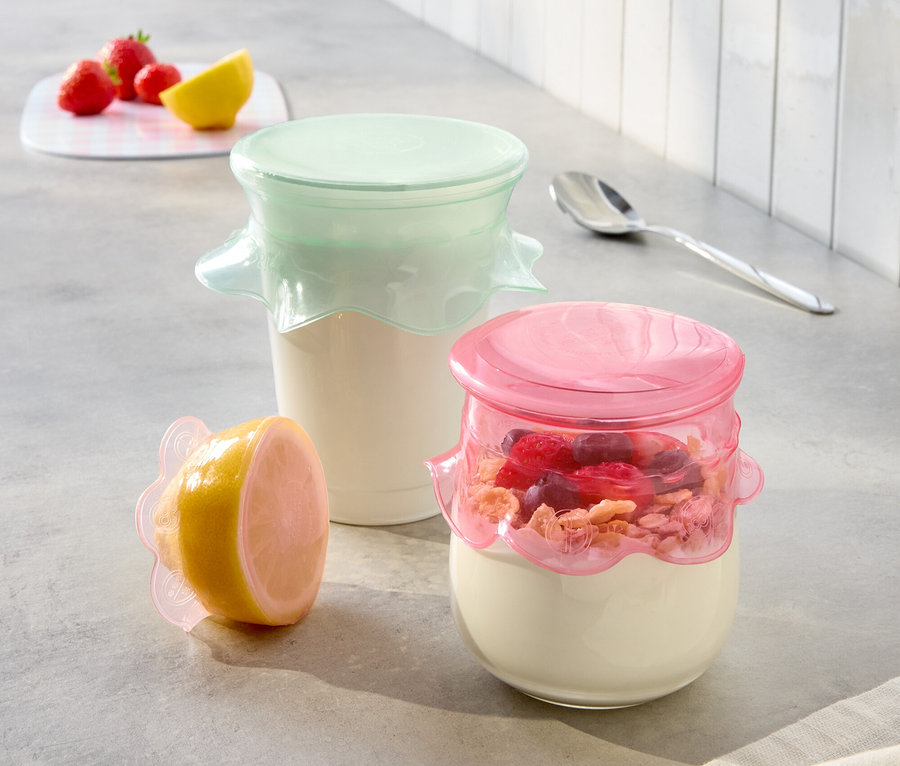 Na kuchyňské lince stojí dvě sklenice jogurtu s růžovými a mátovými víčky a půlka citronu s růžovým víčkem.