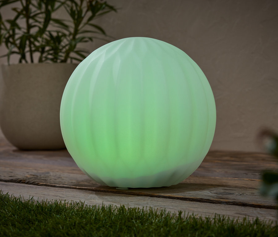 Zelená kulovitá lampa stojí na dřevěném povrchu vedle hrnkové rostliny.