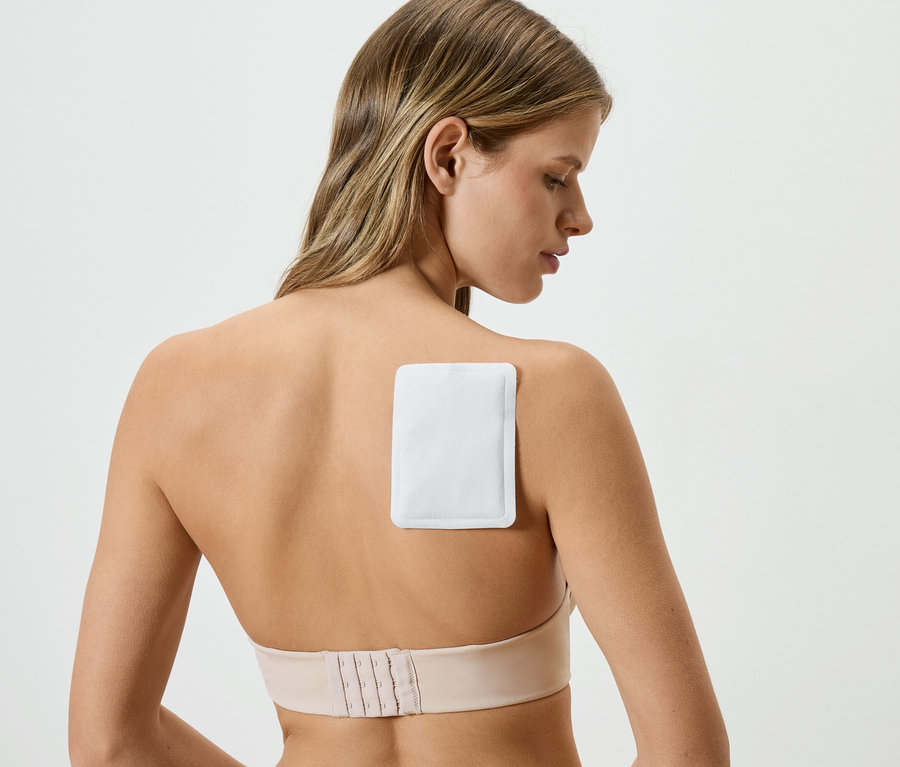 Žena s hřejivou náplastí na zádech, má na sobě tělovou podprsenku.