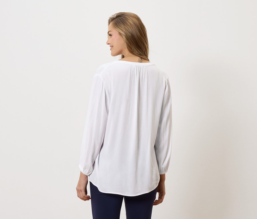 Žena zezadu, má na sobě dlouhou bílou halenku a modré kalhoty.