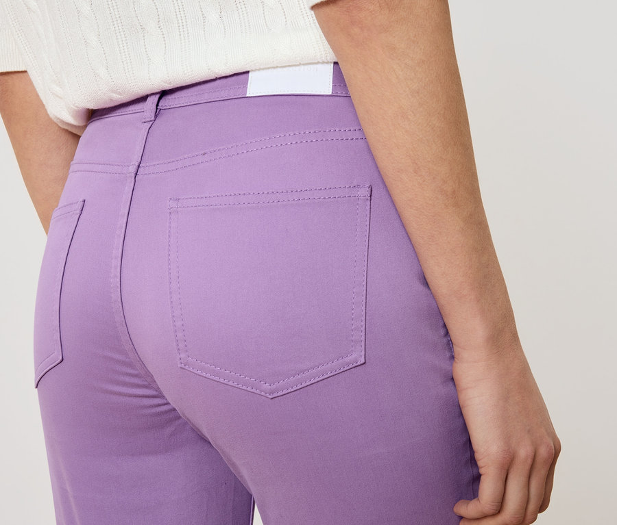 Detailní záběr ženy zezadu v fialových kalhotách a bílém topu.