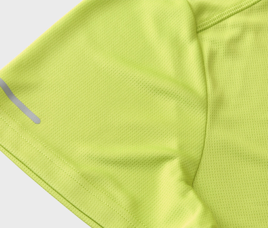 Detailní záběr na rukáv světle zeleného sportovního trička s reflexním pruhem.