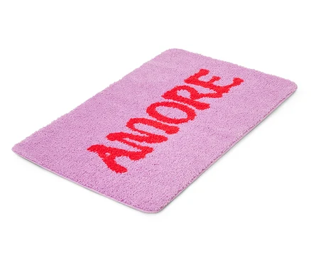 Fialový koupelnový kobereček s červeným nápisem „AMORE“.