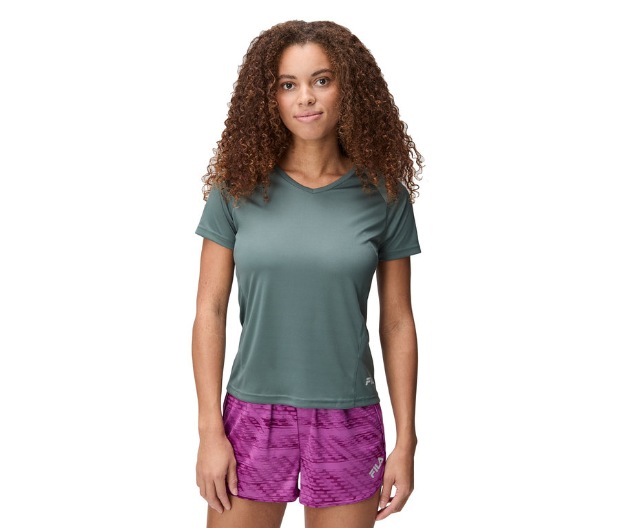 Žena s kudrnatými vlasy má na sobě šedé tričko a růžové šortky.