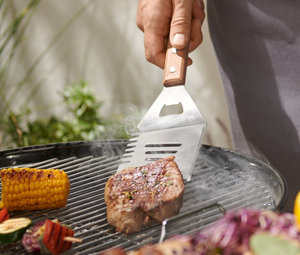 Muž griluje steak pomocí multifunkčního BBQ náčiní.