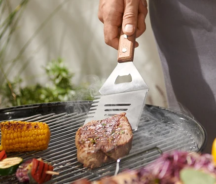 Muž griluje steak pomocí multifunkčního BBQ náčiní.