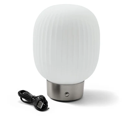 LED akumulátorová stolní lampa se skleněným stínítkem stojí vedle černého nabíjecího kabelu.