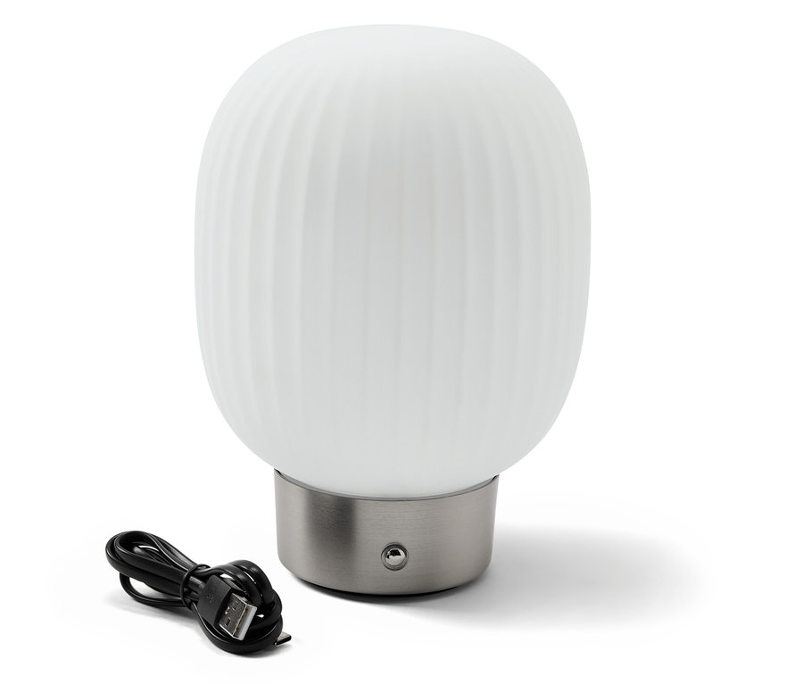 LED akumulátorová stolní lampa se skleněným stínítkem stojí vedle černého nabíjecího kabelu.