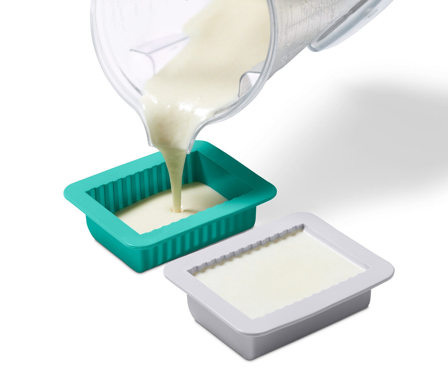 Tekutina se lije z odměrky do zelené formy ze sady na výrobu domácího rostlinného másla. Šedá forma je naplněná.