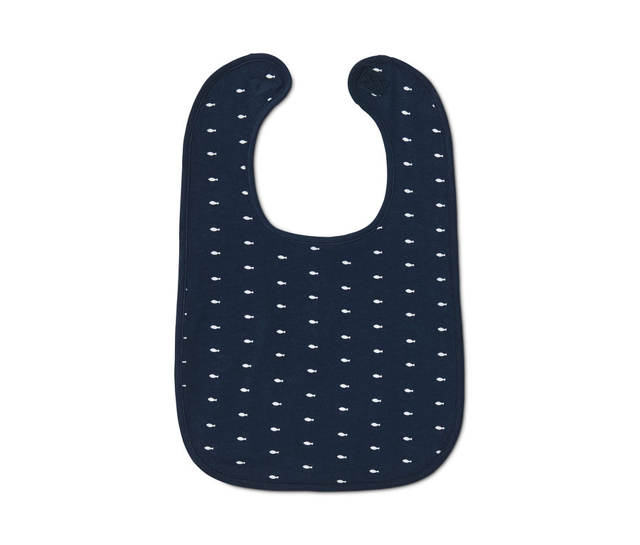 Detail bavlněného bryndáčku s potiskem malých bílých ryb na tmavě modrém pozadí.