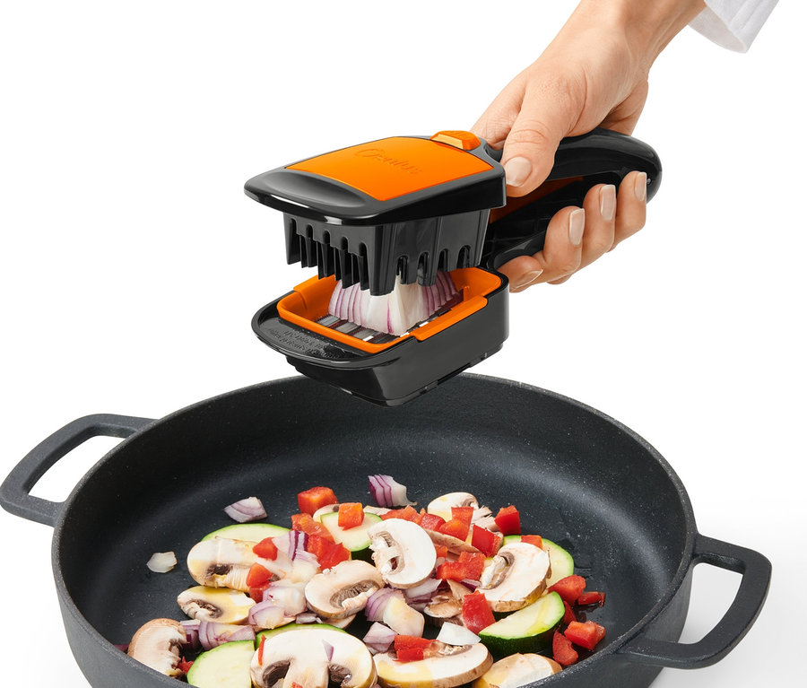 Ruka používá Nicer Dicer Quick XXL ke krájení cibule nad pánví se zeleninou.