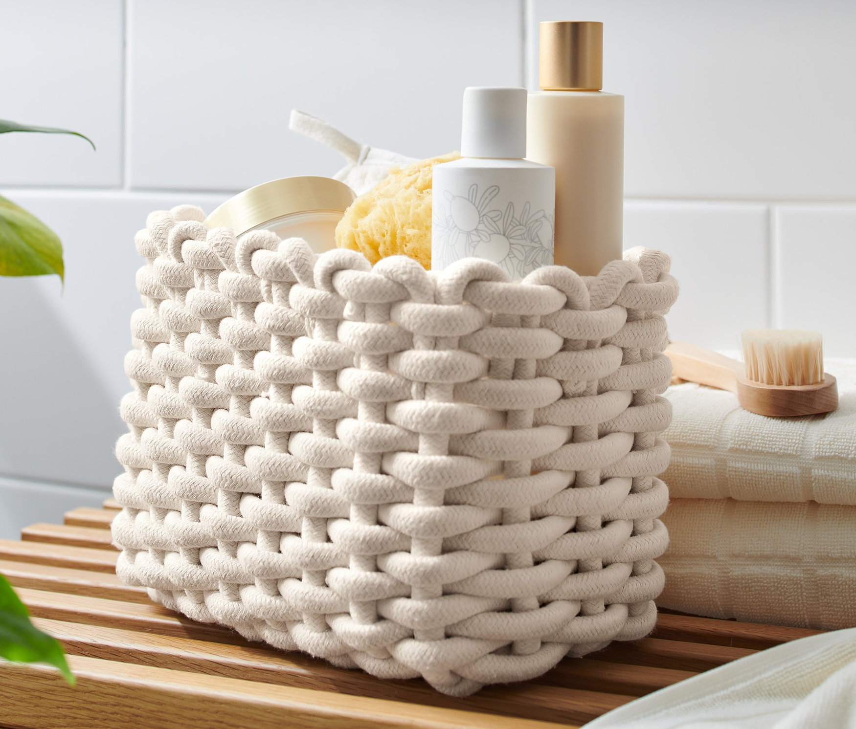 Pletený košík stojí na dřevěné polici vedle složených ručníků.