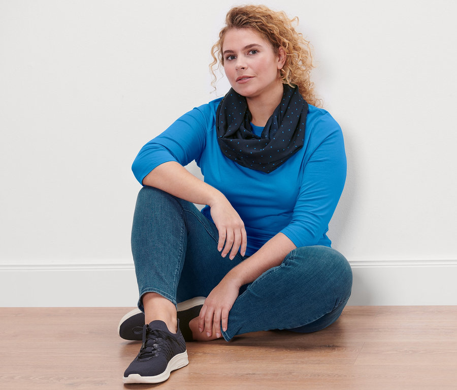 Žena sedí na podlaze a má na sobě azurově modré triko s tříčtvrtečním rukávem, tregíny Fit Nelly a kruhovou šálu s puntíky.