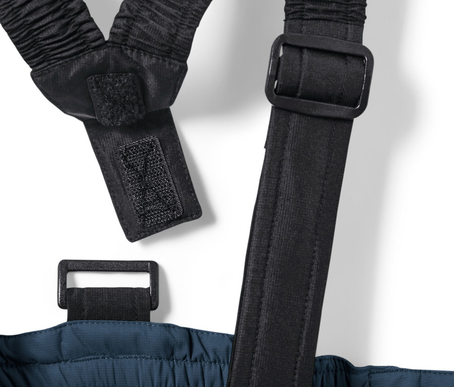 Detail dětských lyžařských kalhot námořnické modré barvy s černými elastickými šlemi a přezkami.