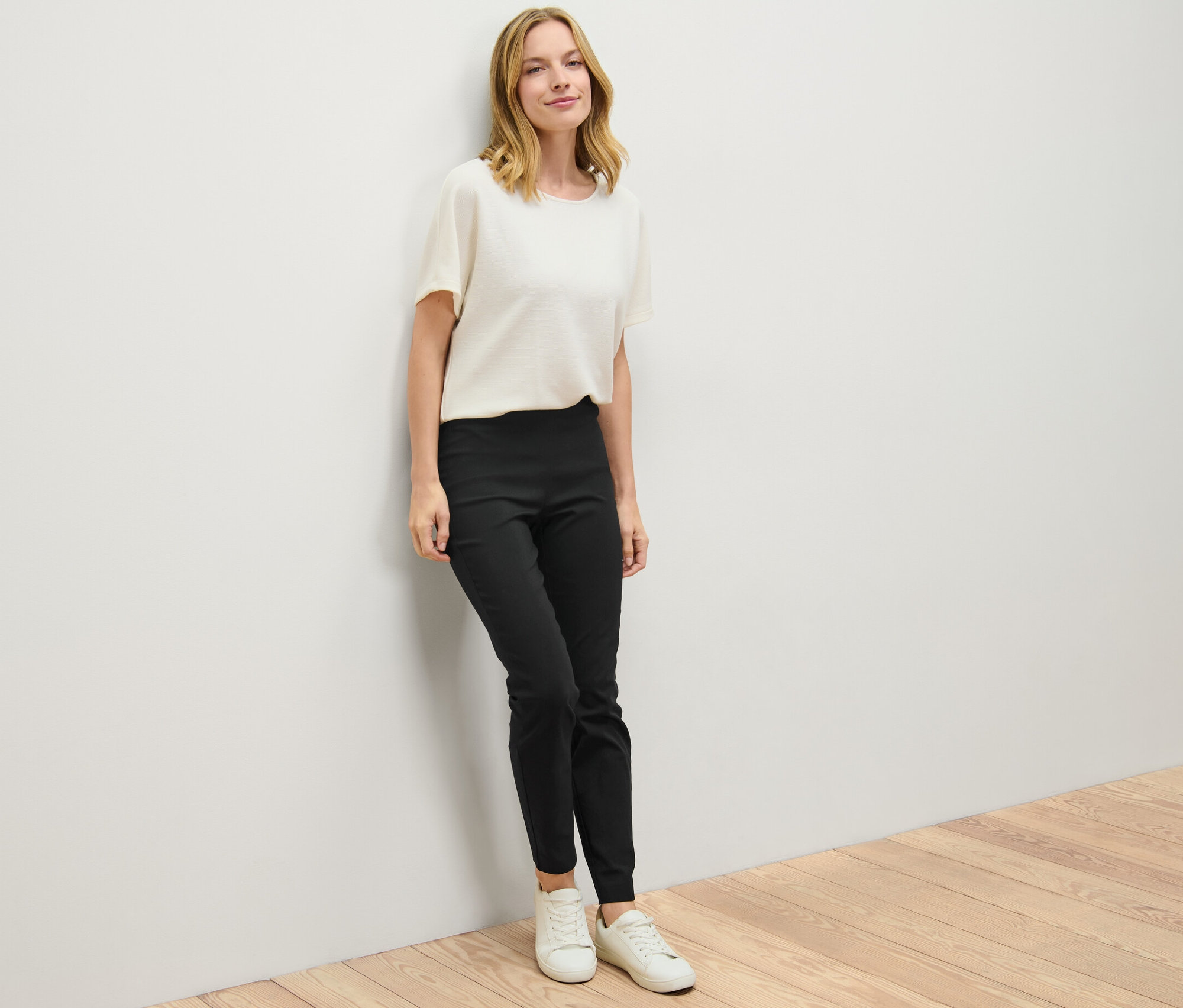 Žena opřená o stěnu má na sobě černé strečové kalhoty.