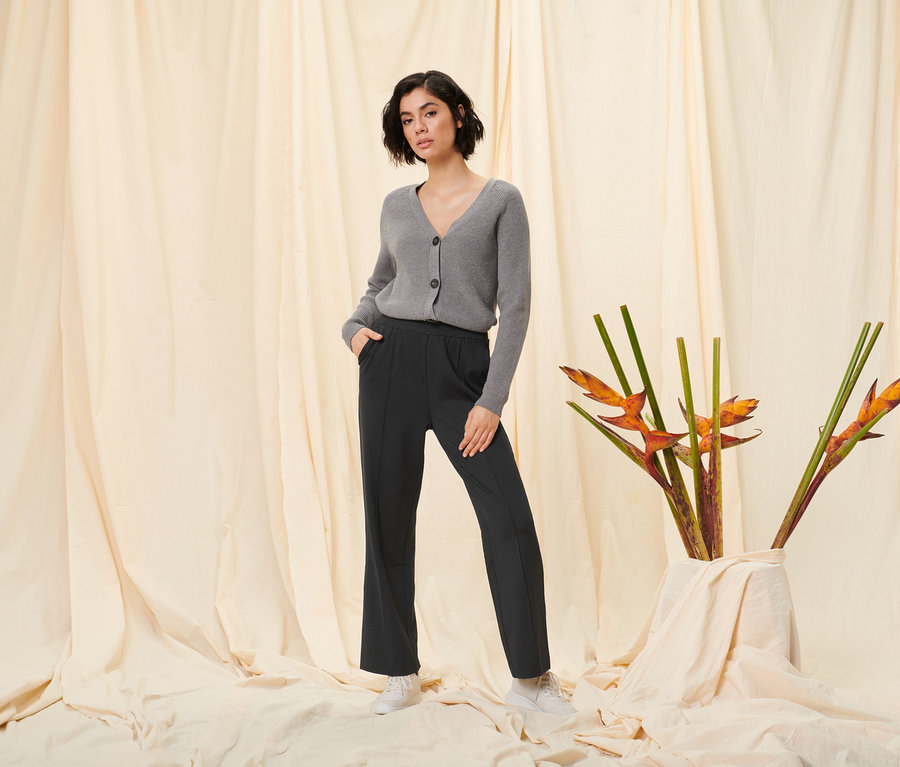 Žena pózuje v černých teplákových kalhotách a šedém kardiganu z hrubé pleteniny.