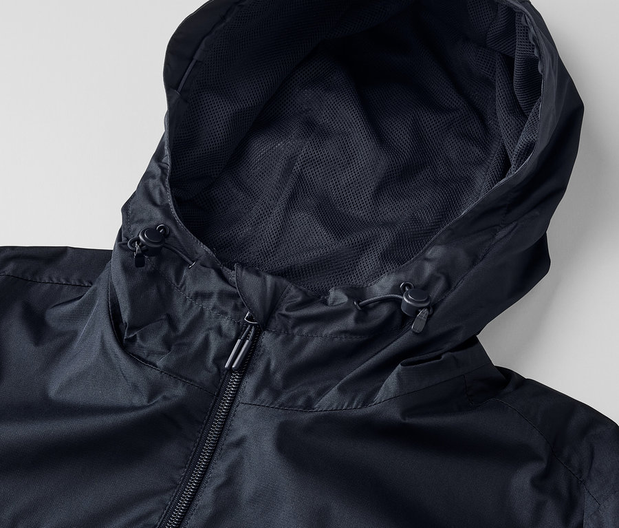 Detail černé unisexové bundy do deště s kapucí a zipem.