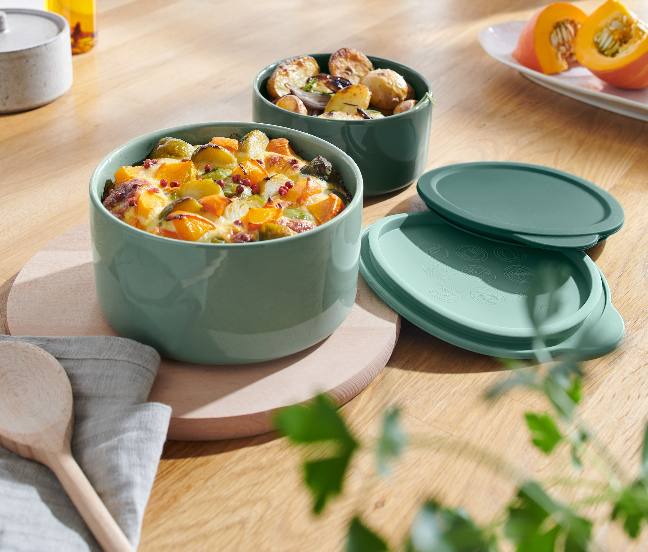 Dvě keramické zapékací mísy s jídlem na dřevěném stole.