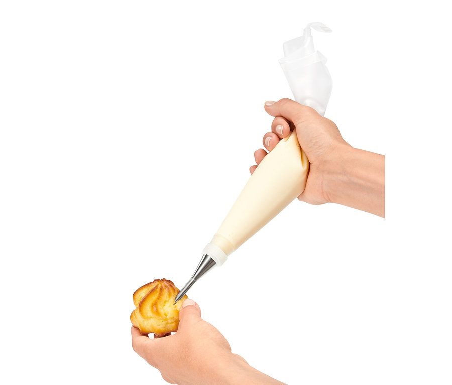 Ruka plní krémem profiterol pomocí sady zdobicích špiček.