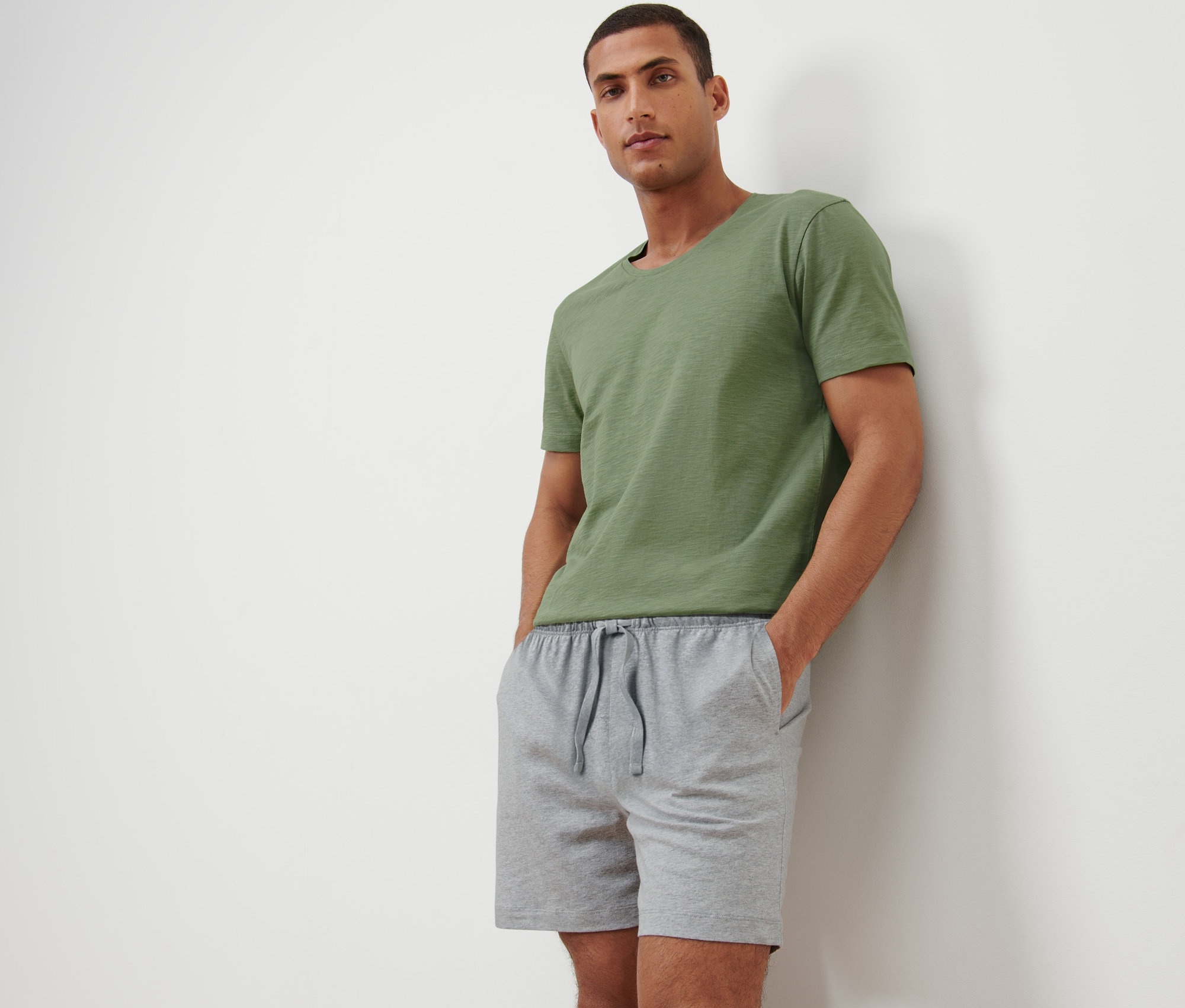 Muž pózuje v krátkém pyžamu a zeleném tričku.