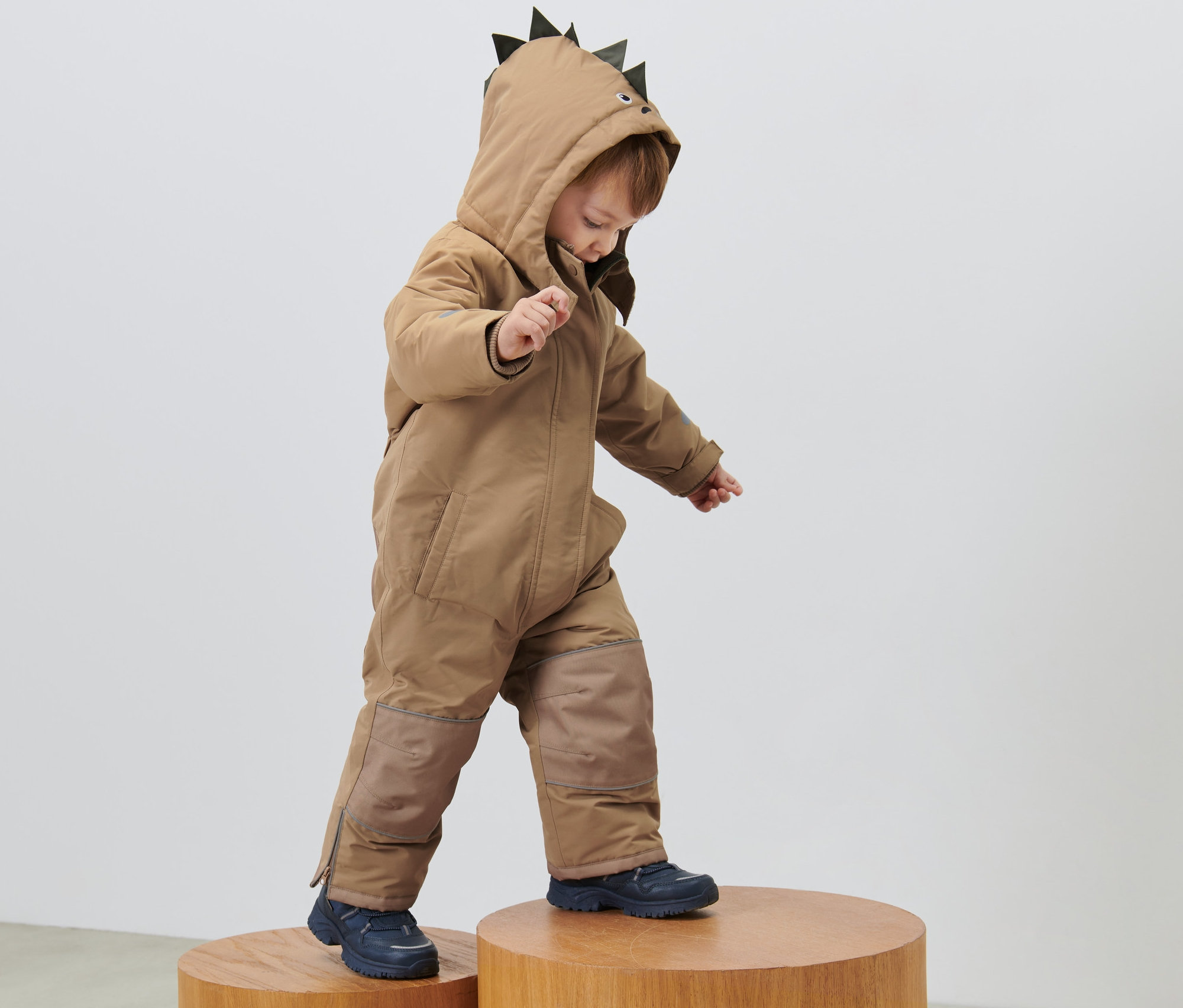 Dítě v dětské zimní kombinéze s kapucí s hroty, stojí na dřevěných stoličkách.