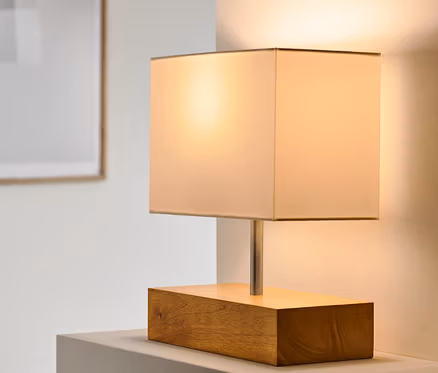 Stolní lampa s dřevěným podstavcem stojí na bílém povrchu.