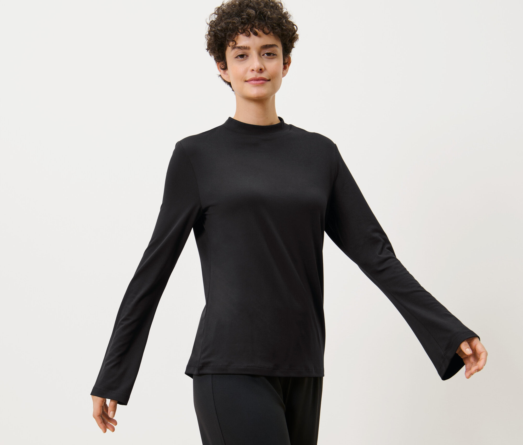 Žena pózuje ve sportovním triku s dlouhým rukávem.