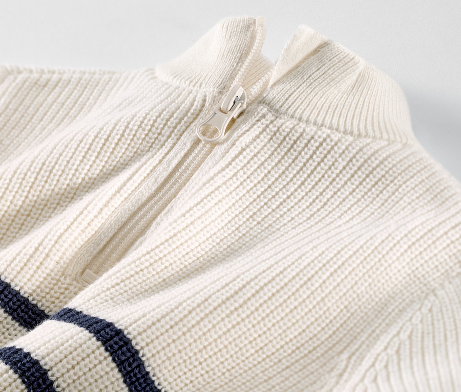 Detailní záběr na dětský svetr troyer s bílým zipem a tmavě modrými pruhy.