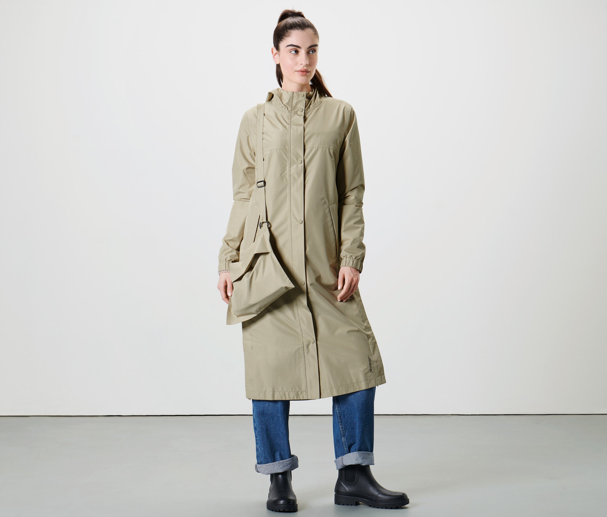 Žena pózuje ve studiu v extra dlouhém béžovém kabátu do deště.