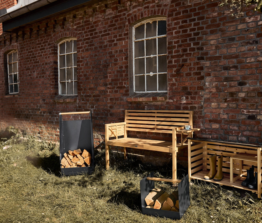 Venkovní botník, dřevěná lavice a dva koše na dřevo stojí na trávníku před cihlovou budovou.