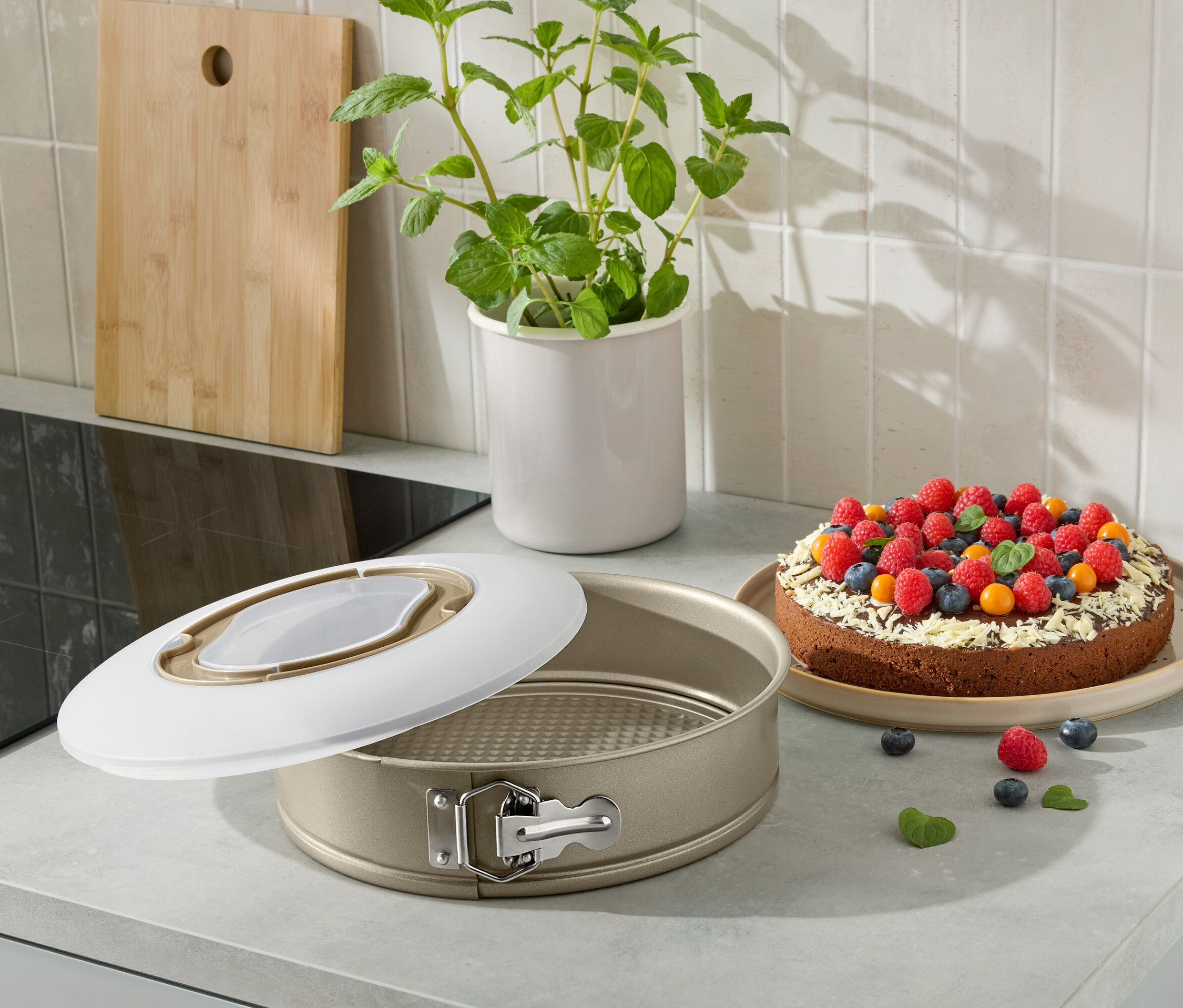 Otevřená forma na dort s upečeným dortem zdobeným ovocem na kuchyňské lince.