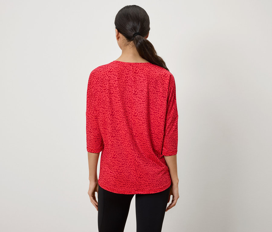 Zezadu je vidět žena s vlasy staženými do culíku, má na sobě červený top s tříčtvrtečními rukávy a zvířecím vzorem.