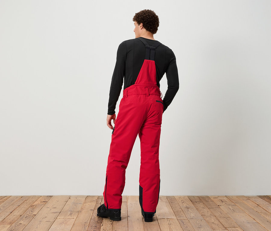 Muž zády k fotoaparátu má na sobě červené lyžařské kalhoty s laclem a černé tričko.