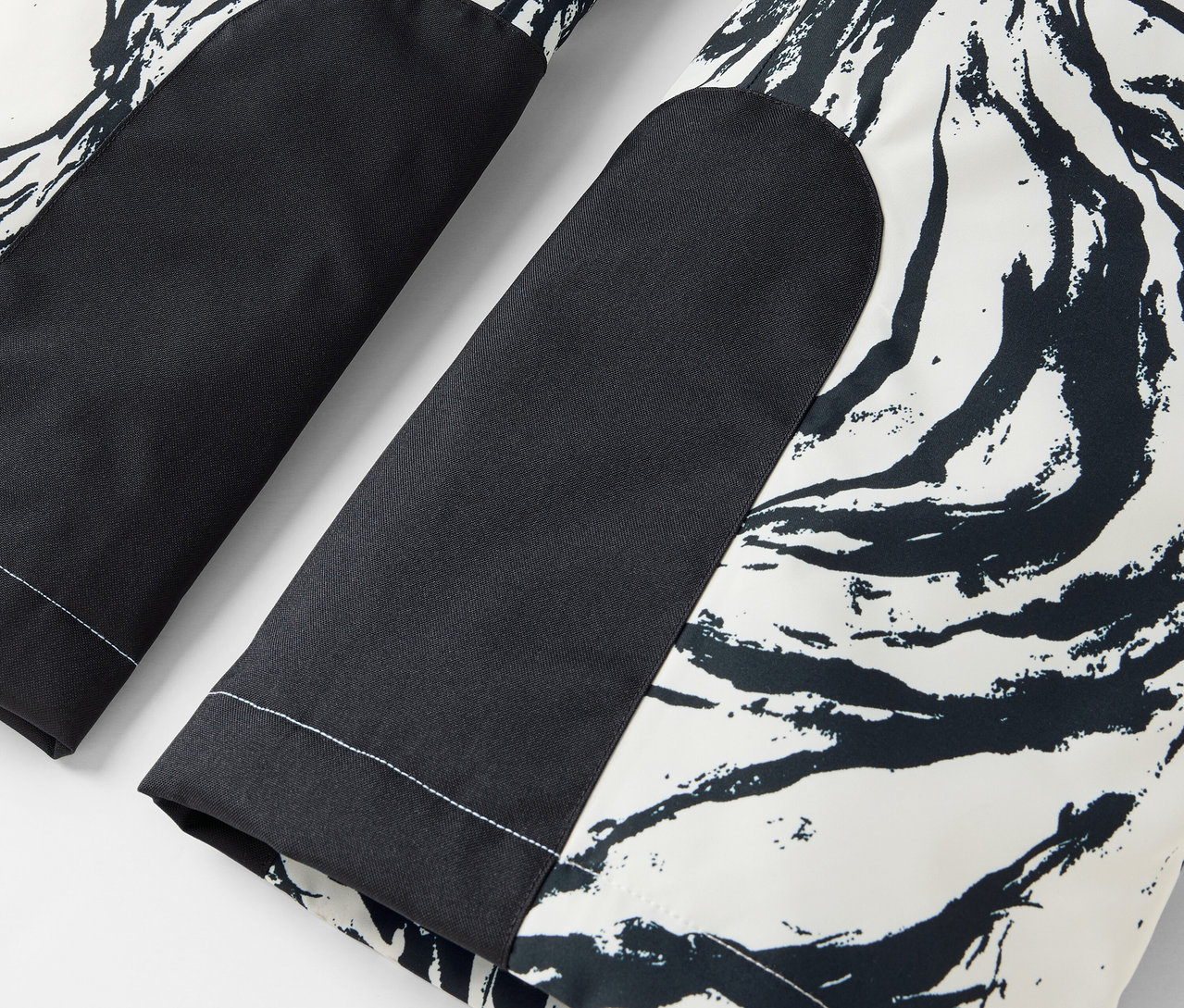 Detail černobílých kalhot s abstraktním vzorem a černými kolenními záplatami.