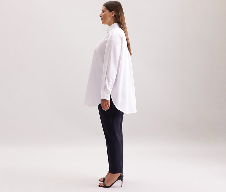 Žena má na sobě bílou halenku oversize Seidensticker, tmavé kalhoty a černé boty na vysokém podpatku.