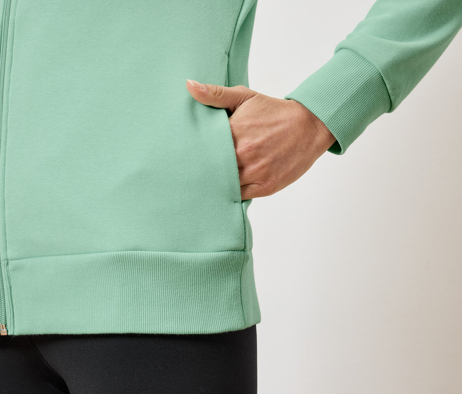 Detail dámské světle zelené mikiny na zip s rukou v kapse.