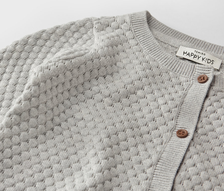 Detail šedého pleteného svetru pro miminka.