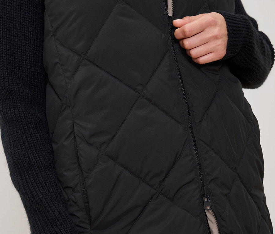 Žena si zapíná černou prošívanou vestu.