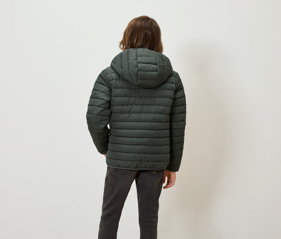Zezadu je vidět osoba s hnědými vlasy v zelené péřové bundě s kapucí a šedých džínách.