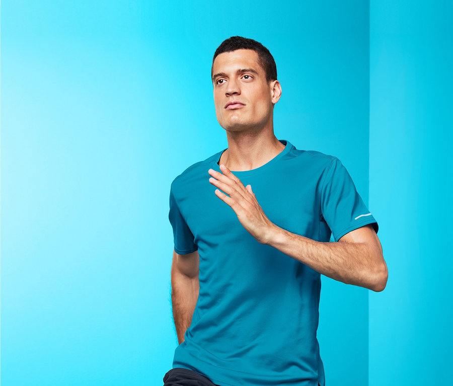 Muž v modrém funkčním triku a černých šortkách běží před modrým pozadím.