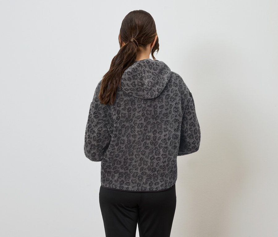 Žena zády k fotoaparátu má na sobě šedou mikinu s kapucí se zvířecím vzorem a černé kalhoty.