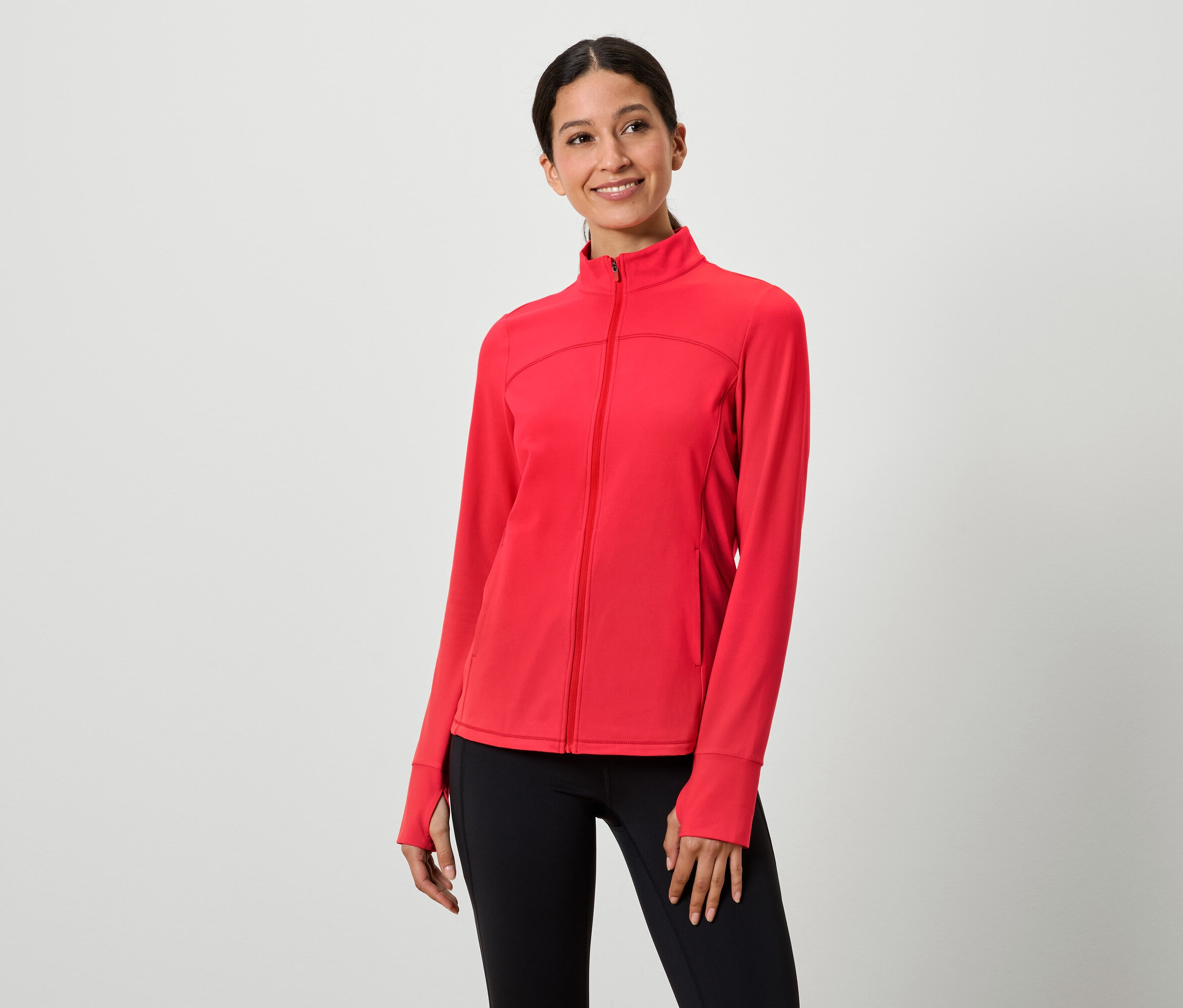Žena má na sobě červenou bundu na zip a černé legíny.