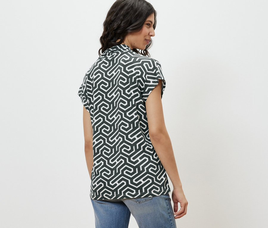 Žena z profilu má na sobě zelené halenkové triko s výstřihem do V a džíny.