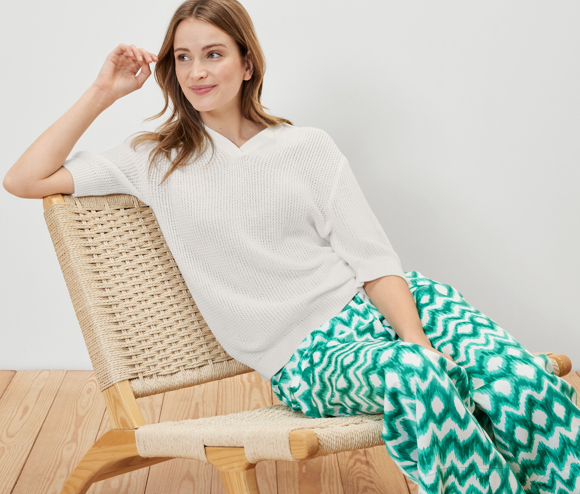 Žena sedí v křesle a má na sobě letní pletený svetr.