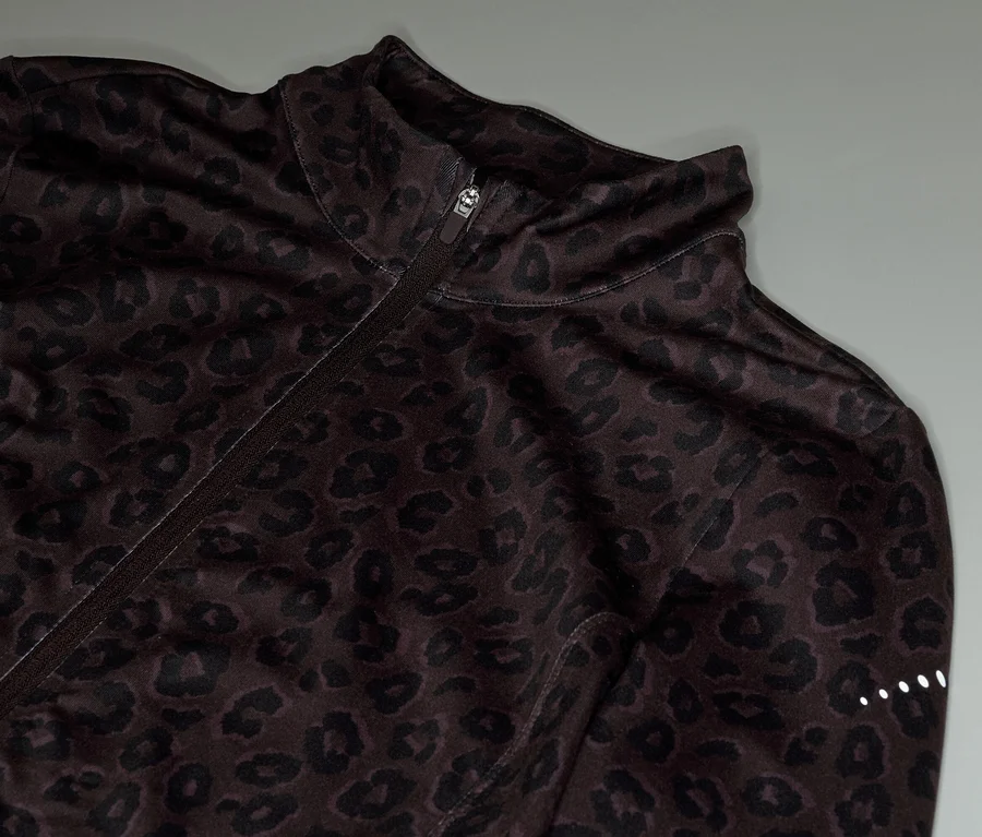 Detail hnědé tréninkové bundy se zipem a leopardím vzorem.